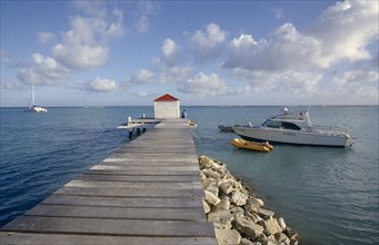 GUADELOUPE, St Froulon, Wooden jetty stretching out to sea with a man sat next to a hut at the end