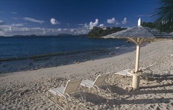 GRENADINES, Mustique, Endeavour Bay. Empty sun loungers on sandy beach with Bequia Island seen from