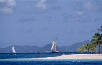 GRENADINES, Petit St Vincent, Palm Island Resort. Man walking on sandy outstretch of beach
