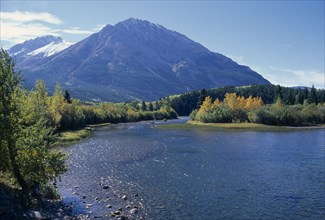 CANADA, Alberta, Landscape near Crowsnest Pass with river flanked by trees in fall colours and snow