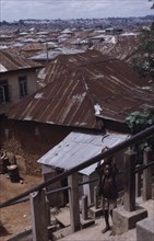 NIGERIA, Ibadan, View across corrugated tin rooftops of city houses with child carrying water jar