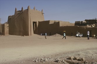 NIGERIA, Kano, Ancient mudbrick city walls and passing people and street trader carrying tray of