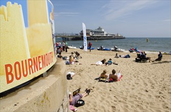 ENGLAND, Dorset, Bournemouth, People lying on the beach on a sunny day with Bournemouth Pier in the
