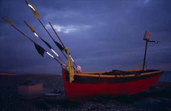 ENGLAND, West Sussex, Worthing, Red and yellow wooden fishing boat pulled up on shingle beach in