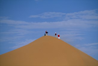 LIBYA, Sahara Desert, Tourists standing on top of Saharan sand dune.