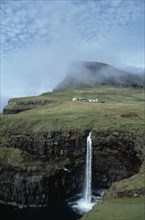 DENMARK, Faeroe Islands, River Gazadalla, Waterfall and rocky coastline with houses built on green
