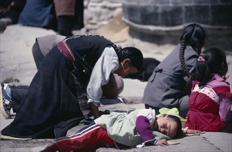 TIBET, Lhasa, Pilgrims at Jokhang Monastery.  Kneeling woman and prostrate child on ground in front