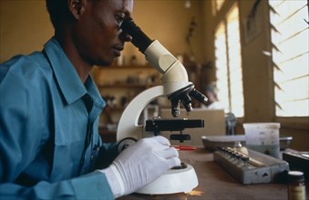 TANZANIA, Health, "Man working in medical laboratory, looking at slides underneath microscope."