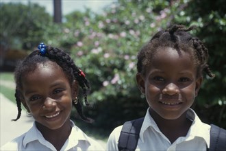 GRENADA, Petit Martinique, Head and shoulders portrait of two smiling schoolgirls with braided hair