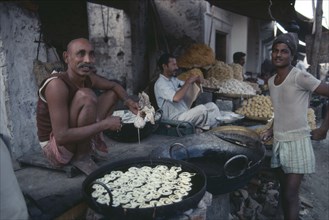 INDIA, Rajasthan, Pushkar, Man cooking fried snacks at pavement food stall.