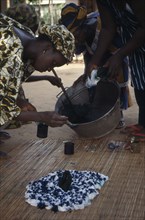 GAMBIA, Arts, Woman applying indigo dye to cloth during tie dye process.