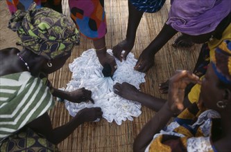 GAMBIA, Arts, Women applying indigo dye to cloth during tie dye process.