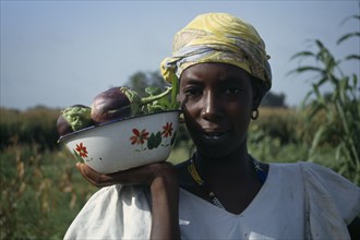 GAMBIA, Agriculture, Head and shoulders portrait of woman holding dish of aubergines.
