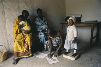 TANZANIA, Health, Nurse in rural area weighing child and making notes on growth chart.