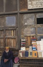EGYPT, Nile Delta, Alexandria, Arab book vendor beside street stall.