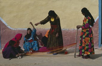 EGYPT, Western Desert, Bedouin, Group of Bedouin women in colourful dress weaving and spinning