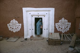 MAURITANIA, Oualata, "Woman stepping out from doorway with white surround and traditional bas