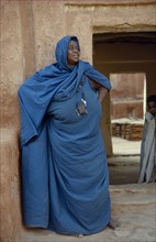 MAURITANIA, Oualata, Portrait of woman wearing turquoise robe and head covering standing in front