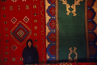 WESTERN SAHARA, SADR, Sahrawi woman standing in front of traditional carpets.