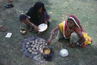 INDIA, Rajasthan, Pushkar, Women cooking over small open fire and hot ashes on the ground.