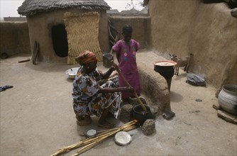 GHANA, Chereponi, "Woman cooking over open stove watched by young girl in small, walled yard with