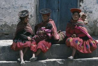 PERU, Cuzco, Ollantaytambo, Women carrying children in blanket slings resting in plaza after walk