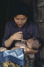 THAILAND, People, Cambodian refugee mother breastfeeding baby while sewing.