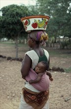 BURKINA FASO, People, Woman carrying baby in sling on her back and painted bowl on her head in area