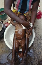 BURKINA FASO, Gourounsi, Cropped shot of mother washing baby girl in bowl in village near Sanone