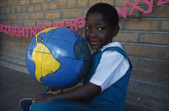MALAWI, Blantyre, Portrait of child holding papier mache globe teaching aid made by PAMET from
