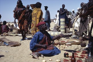 CHAD, Markets, Kanimbo market with woman sat on ground selling foodstuffs with people standing