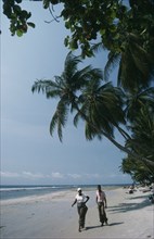 GABON, Landscape, Cape esteries. Man and woman walking along sandy beach lined with overhanging