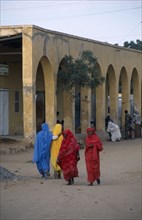 ERITREA, Tessanie, Women in colourful muslim clothing walking along road near a yellow building