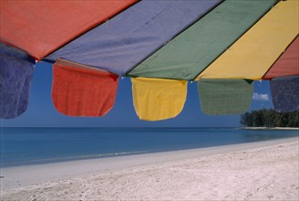 THAILAND, North Phuket, Naiyang Beach, Close up of a multi coloured parasol on the sandy beach.