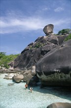 THAILAND, Koh Similan  , Sail Rock, A couple walking in the water at the base of the large rocks.