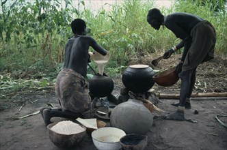 SUDAN, Tribal People, Dinka women cooking millet and sorghum in pots over open fire.