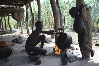 SUDAN, Tribal People, Dinka children cooking over open fire beneath house raised above ground level