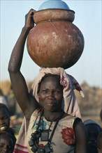 SUDAN, Momei Settlement, Chadian refugee carrying water pot on her head in camp near El Geneina