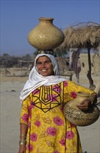 PAKISTAN, Sindh Province, Gurmani, "Woman collecting water, carrying one pot on her head and