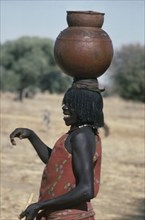 SUDAN, Habila Settlement, Laughing Chadian refugee woman carrying water pot on her head.