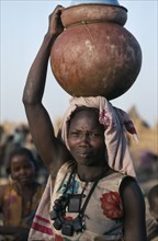 SUDAN, Mornei Settlement, Chadian refugee woman carrying water pot on her head.