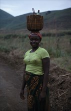 CAMEROON, People, Women, Portrait of young woman carrying woven basket on her head.