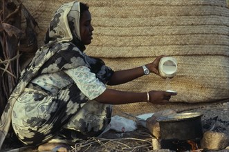 SUDAN, Red Sea Hills Province, Beja nomad woman cooking mededa gruel made from sorghum over open
