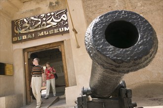 UAE, Dubai , Entrance to the Museum with a cannon to one side and a couple walking through door.