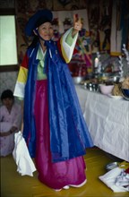 SOUTH KOREA, Religion, Shamanism, Female Shaman with arm raised in air at a funeral wearing
