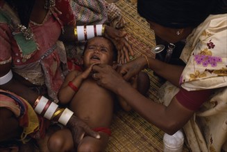 INDIA, Andhra Pradesh, Female health visitor examining tribal baby.