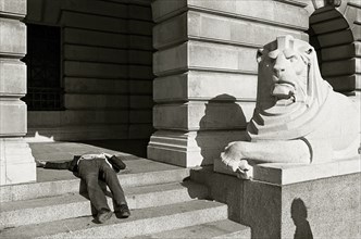 ENGLAND, Nottinghamshire, Nottingham, A drunk sleeps on the steps next to a lion statue outside the
