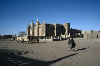 MALI, Sahel, Djenne, Grand Mosque.  Exterior with passer by casting long shadow.