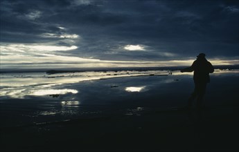 ARCTIC, Landscape, Silhouette of person holding fishing pole with dark sky reflected in the water.