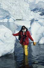 ANTARCTICA, Paradise Harbour, A tourist with camera stands in the water next to icebergs in
